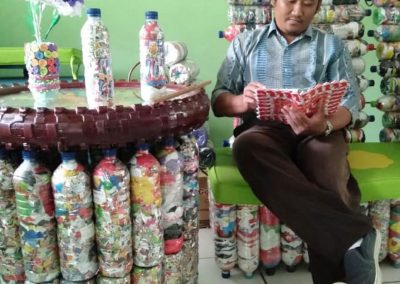 Ood Lantip, reads a book on his Ecobrick courch, beside his ecobrick table in Semarang, Central Java, Indonesia.
